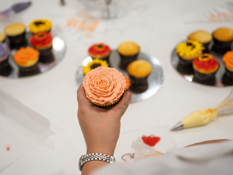 Hand holding a cupcake with buttercream rose on top